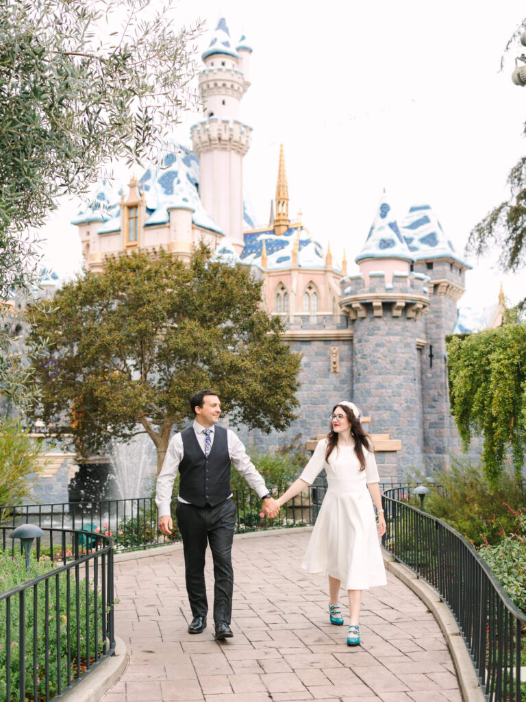 A couple walks hand in hand near a Cinderella Sleeping Beauty castle with blue and gold accents.