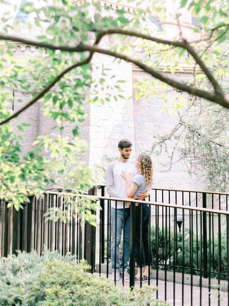 A couple embraces lovingly on a quaint outdoor bridge, surrounded by lush greenery and stone walls