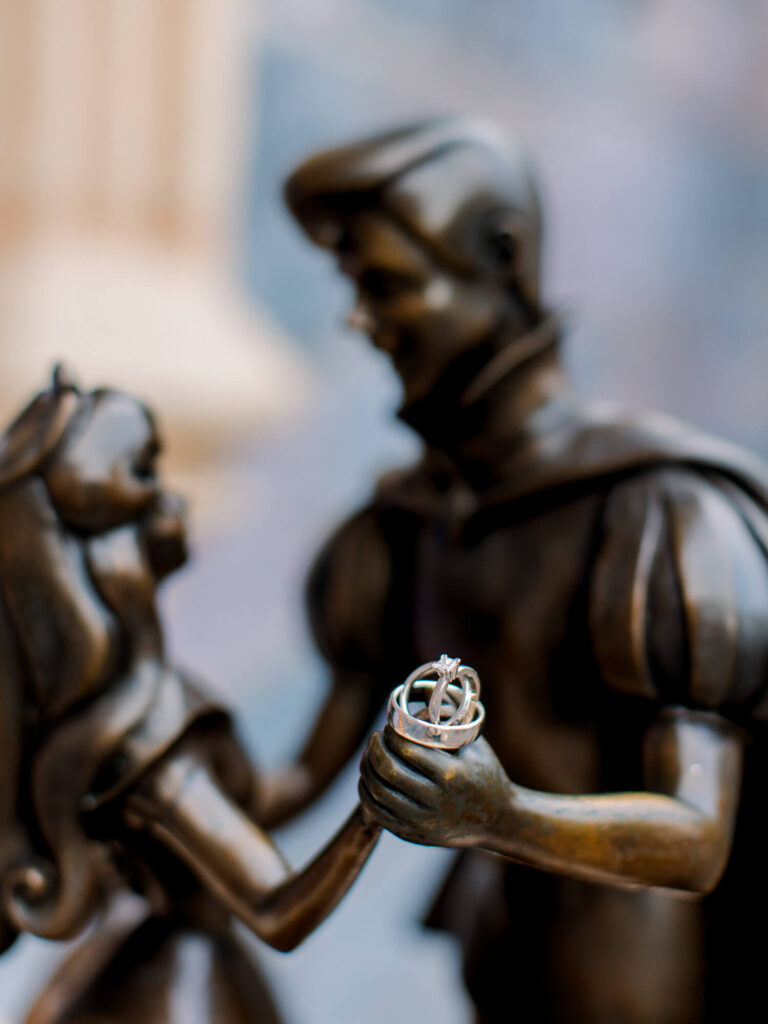 A bronze statue depicts a prince and princess gazing at each other. The prince is holding a ring.