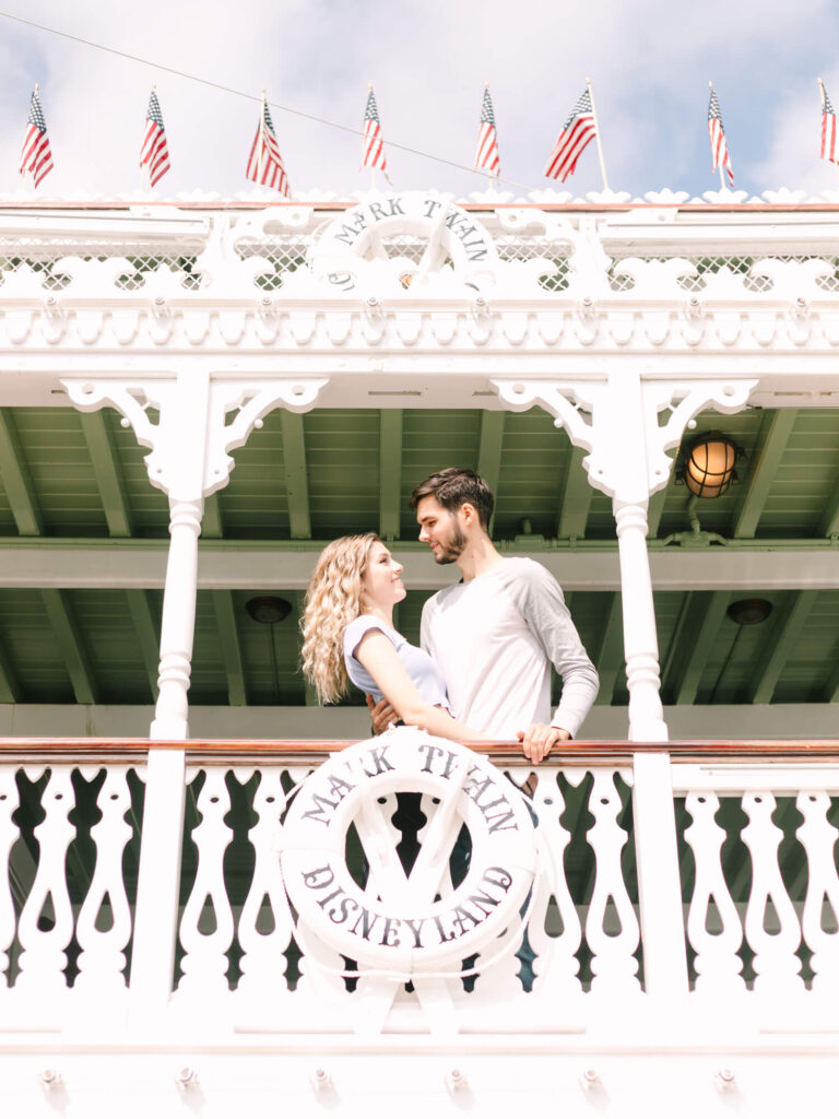 A couple stands on the ornate deck of the Disneyland Mark Twain Riverboat, sharing a loving gaze.