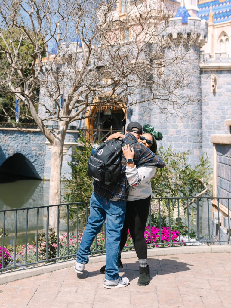 A couple embraces in front of a stone castle at Disneyland theme park.