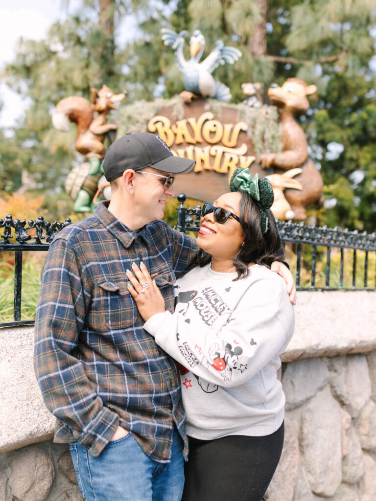 A smiling couple poses in front of a themed park sign reading "Bayou Country." They are casually dressed.