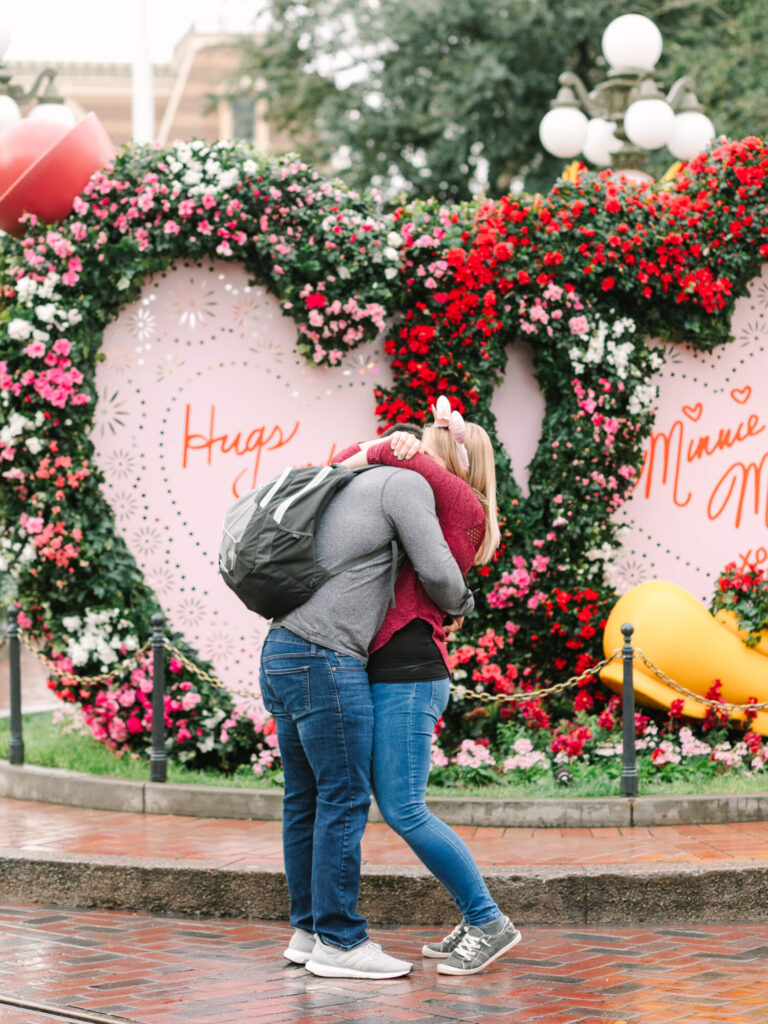 A couple embraces in front of pink heart-shaped flower arches with colorful blooms.