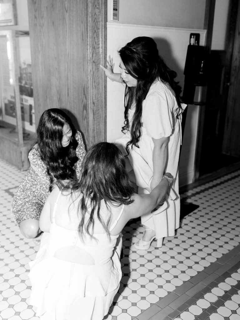 Three women in a black-and-white photo interact in a hallway with tiled flooring