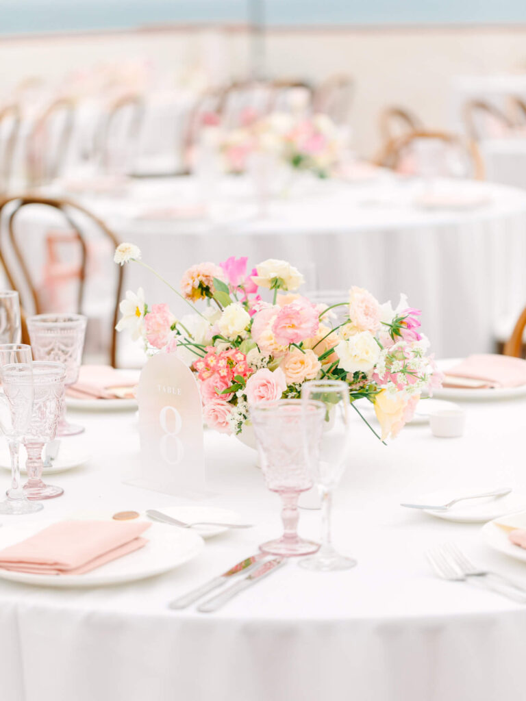Elegant table setting with a floral centerpiece of pink and white flowers on a round table.
