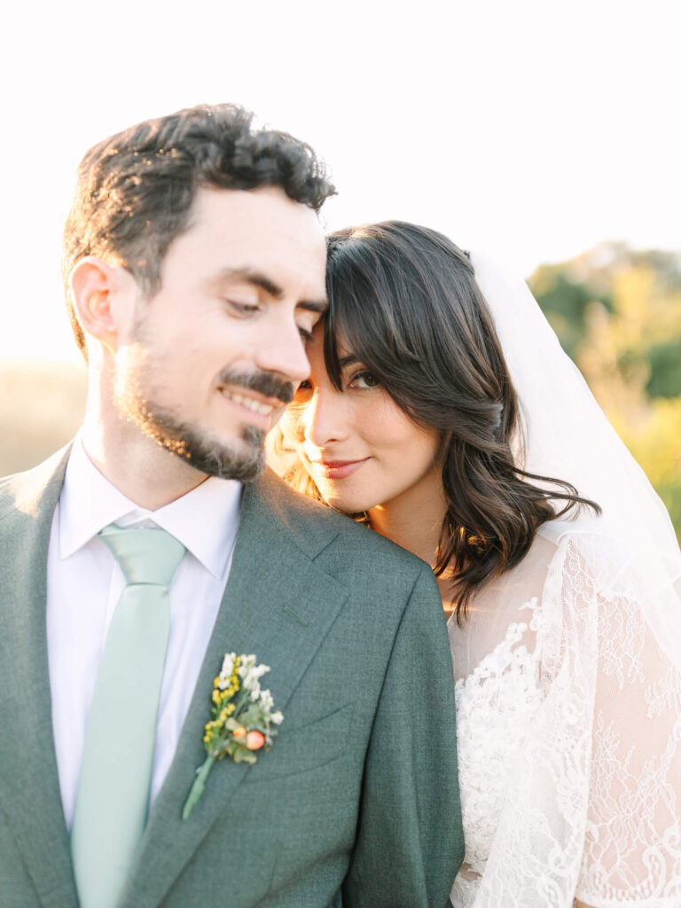 A bride in a white lace dress leans affectionately on the groom's shoulder.