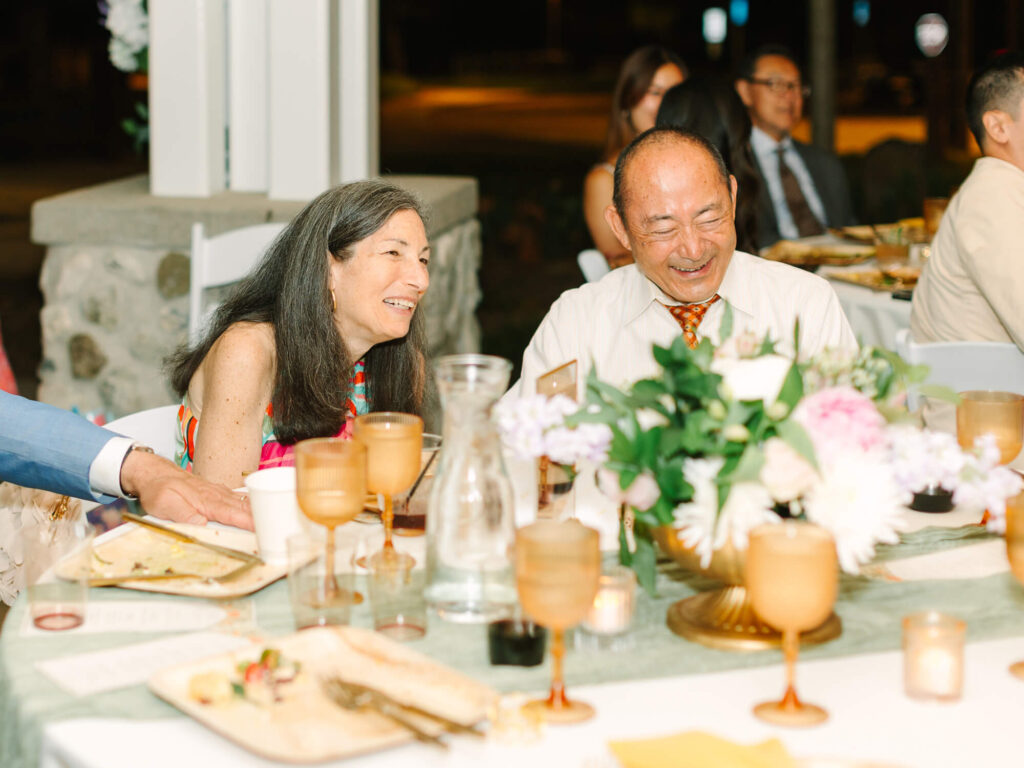 An older couple smiling and laughing at a wedding reception table.