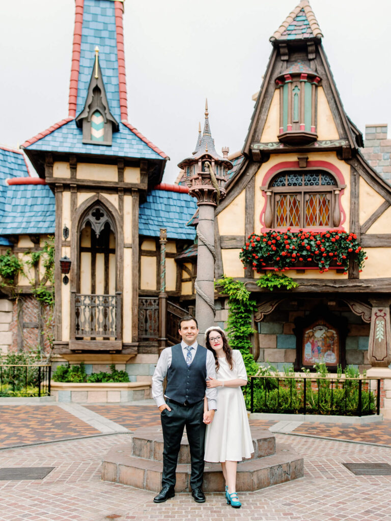 A couple stands together in front of a whimsical, fairytale-style building at Disneyland.