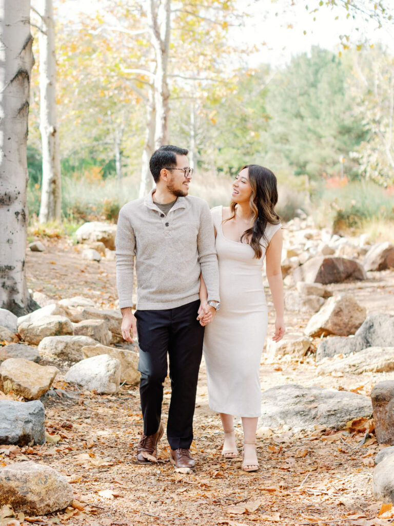 A couple joyfully holds hands while strolling on a leaf-strewn path in a serene park.