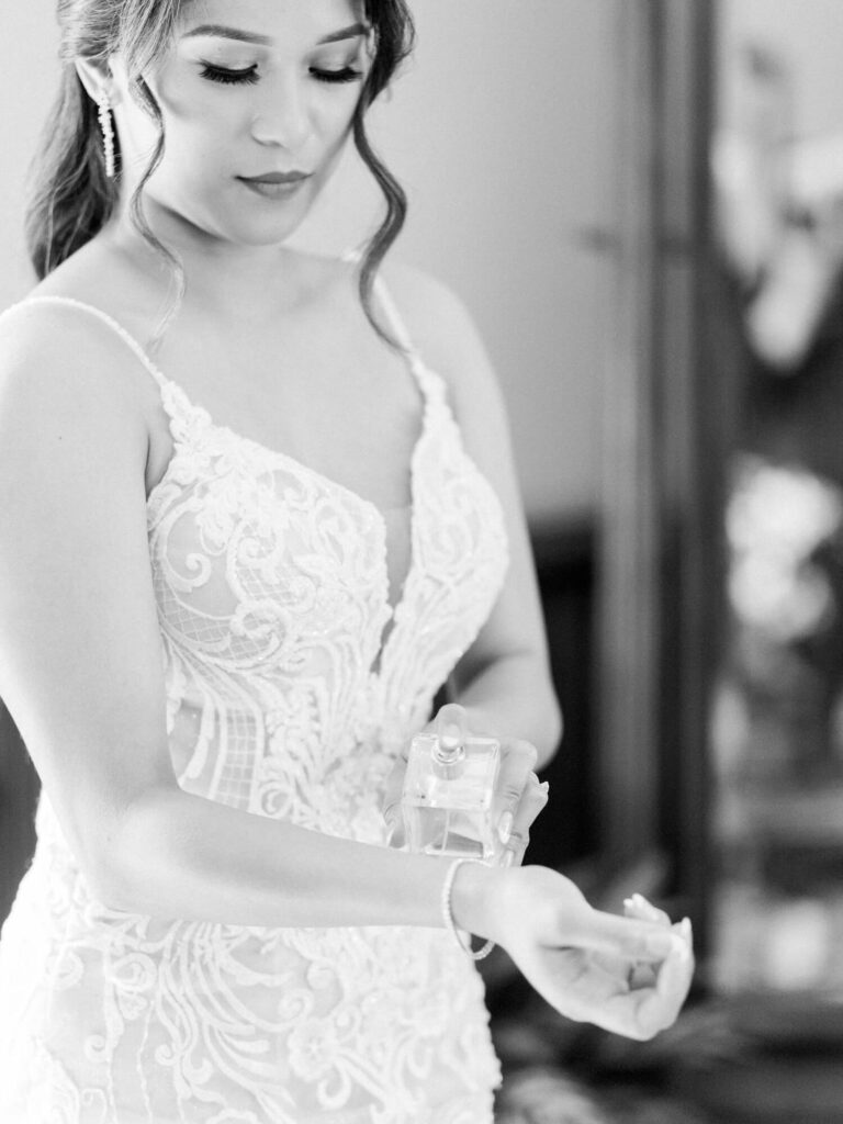 A bride in an elegant lace wedding dress applies perfume to her wrist.