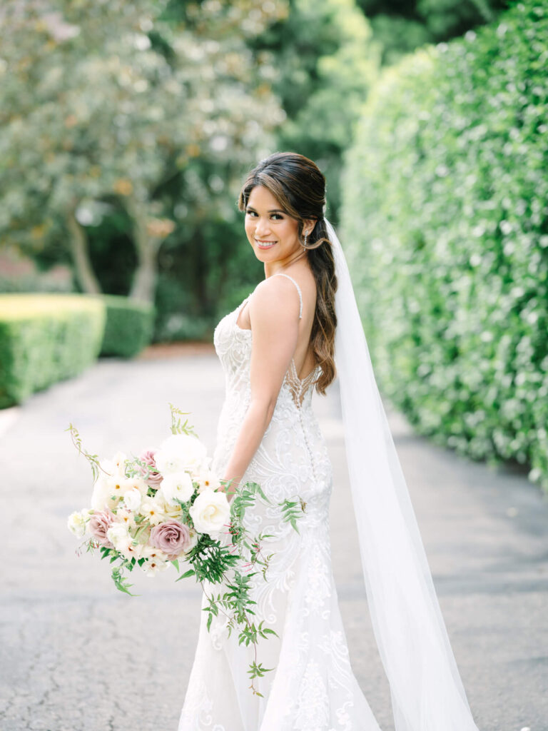 Bride smiling in a lace wedding dress holding a bouquet of white and blush flowers.