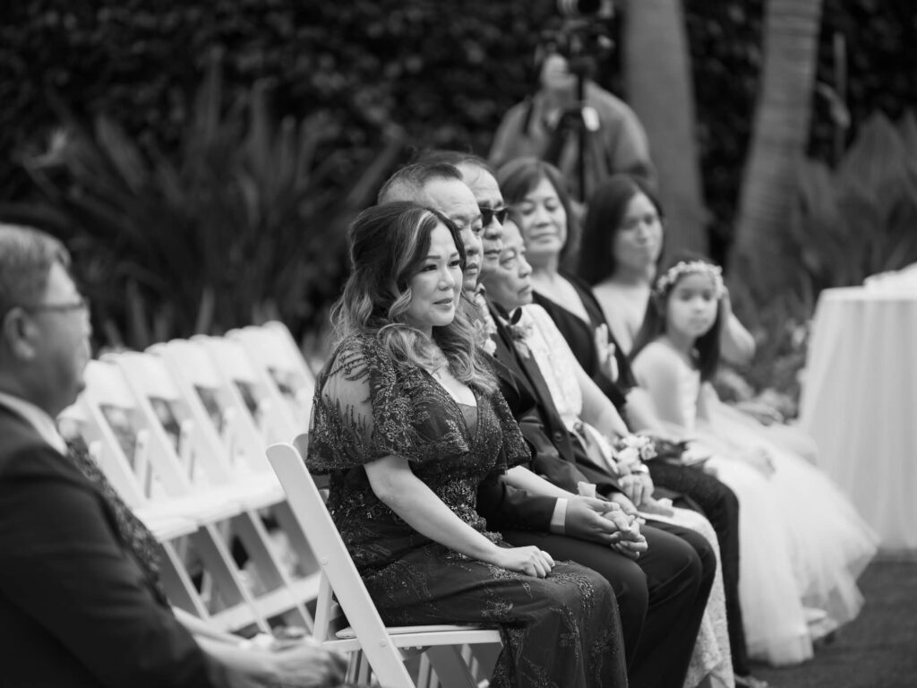 Guests sit in elegantly arranged rows at an outdoor event, wearing formal attire.