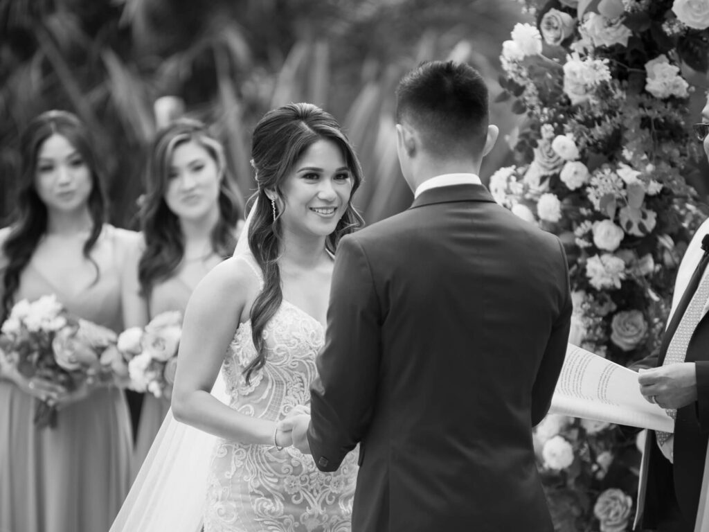 Bride and groom exchange vows at an outdoor wedding. The bride smiles warmly.
