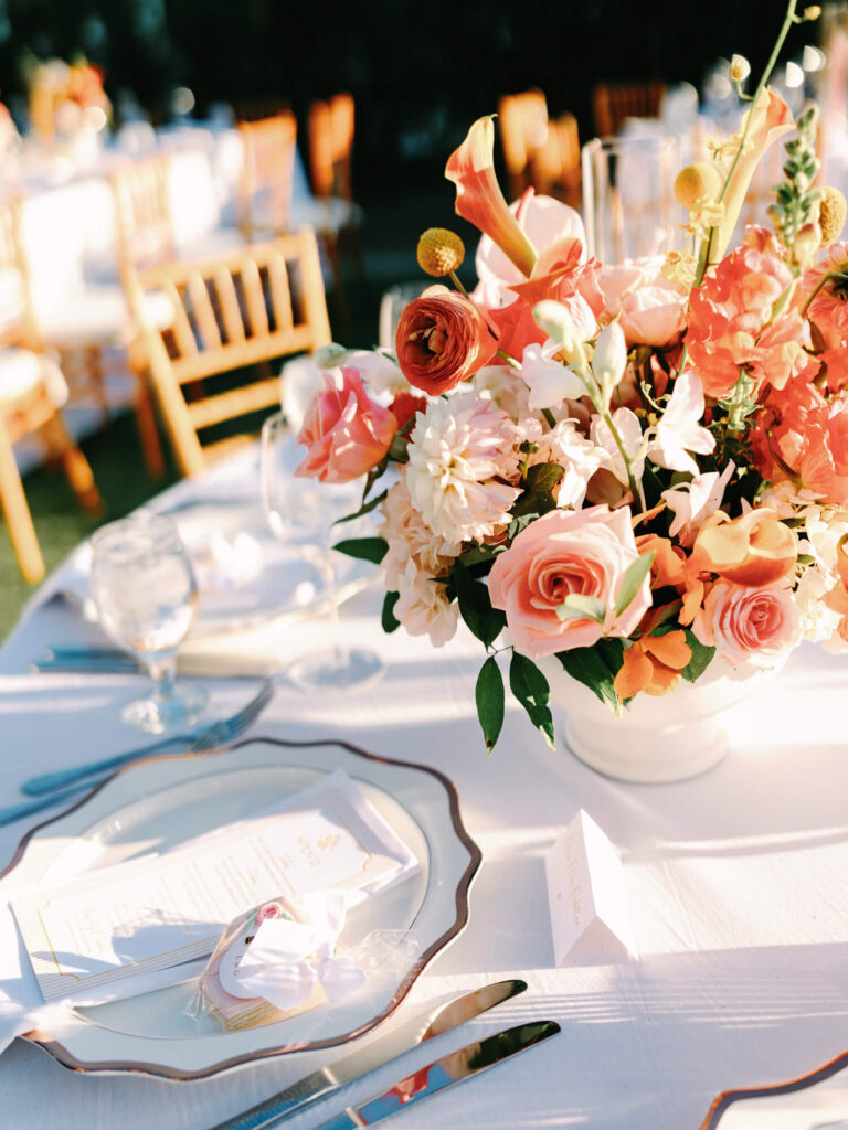 Elegant table setting with a vibrant floral centerpiece of pink and orange flowers.