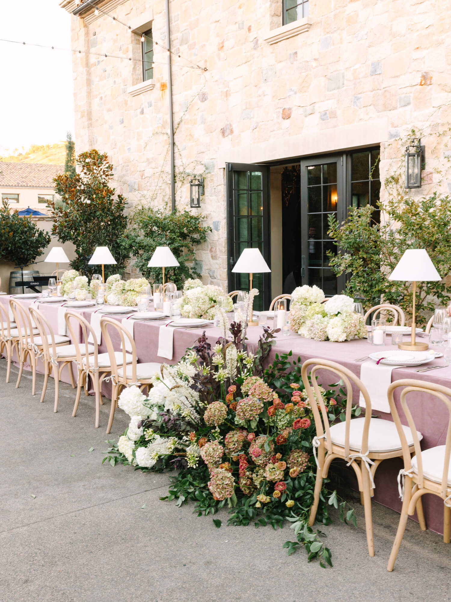 Elegant outdoor table setup with white chairs, lilac tablecloths, and white flowers.