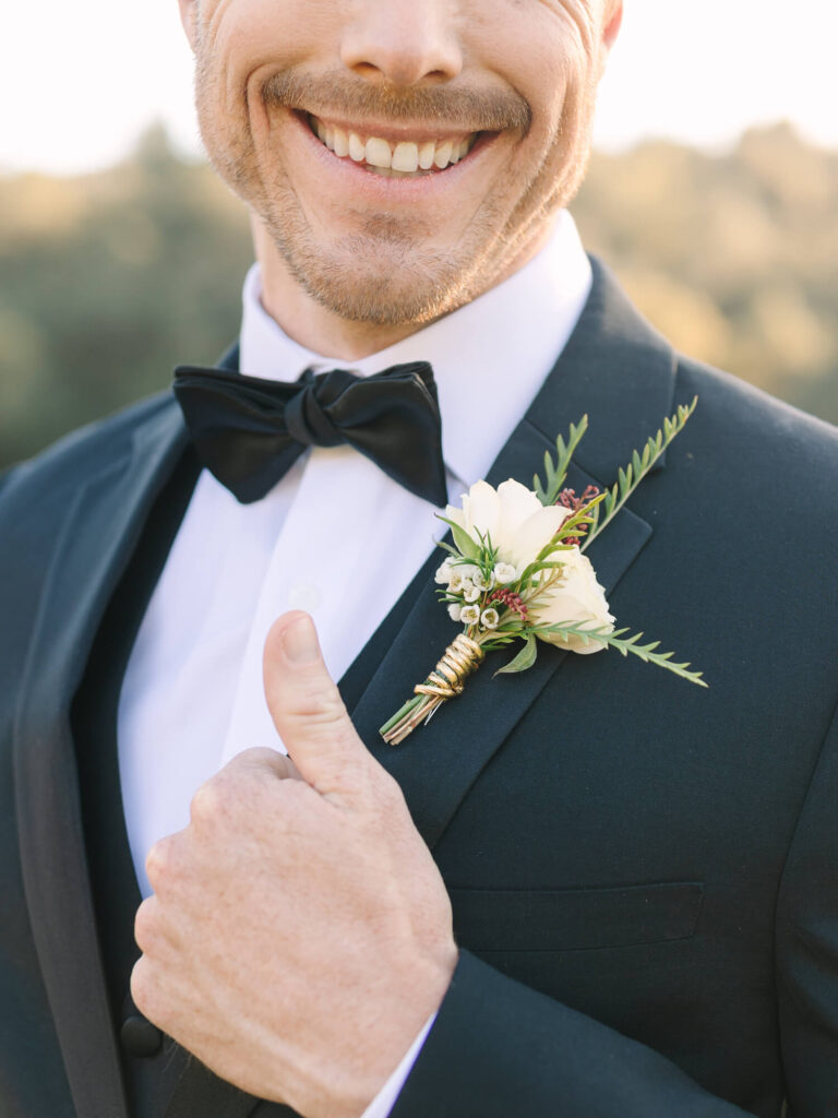 Smiling groom in a suit with a black bow tie and white boutonniere.