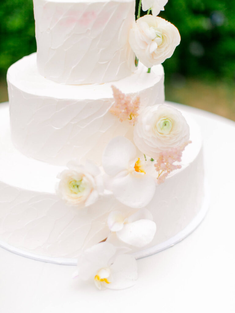 Three-tiered white wedding cake with textured icing, adorned with delicate white and pink flowers.