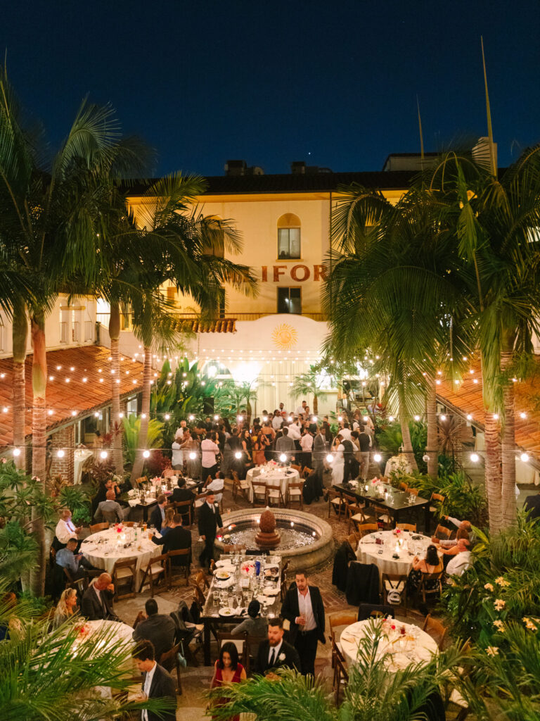 Elegant outdoor evening event at a courtyard with string lights, round tables, and a central fountain.