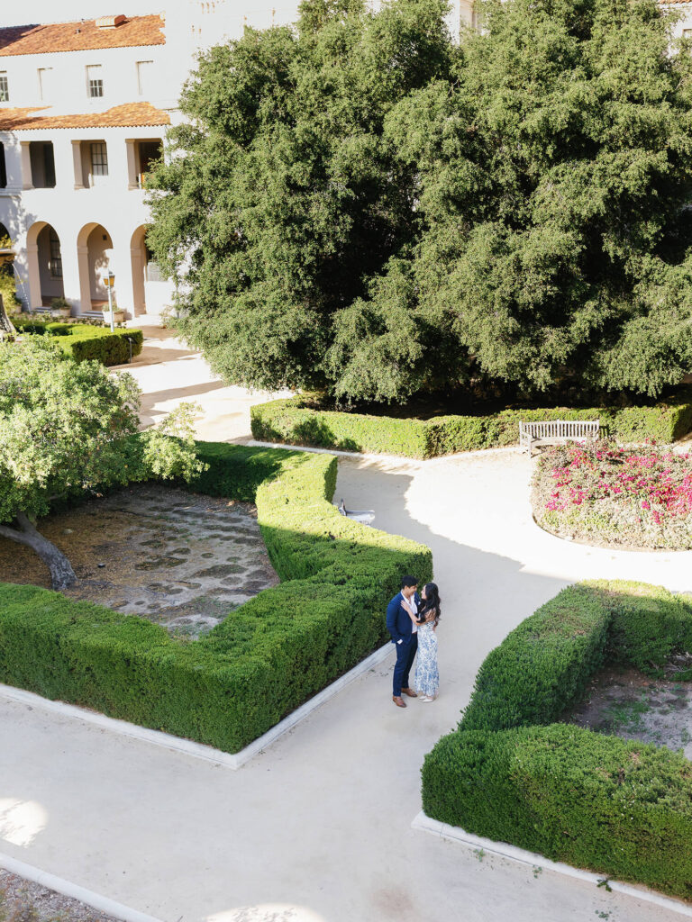 Aerial view of a couple embracing in a neatly landscaped garden with vibrant greenery.