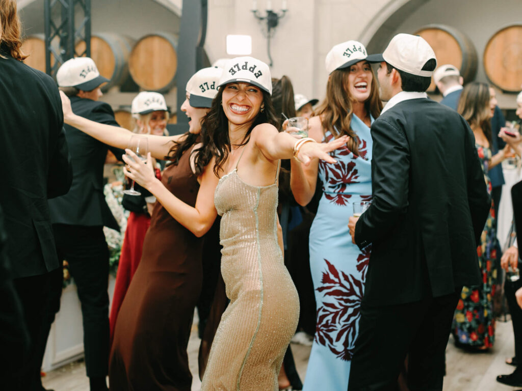 A joyful woman in a glittery dress and white cap dances at a lively party.