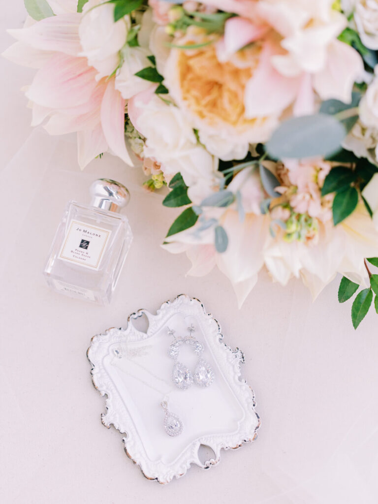 Elegant arrangement featuring a delicate bouquet of pink and white flowers, a bottle of perfume, and sparkling jewelry on a decorative tray.