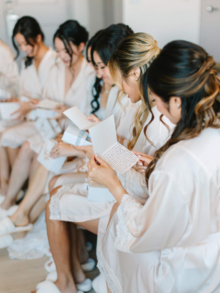 A group of women in matching white robes sit in a row, reading heartfelt letters.