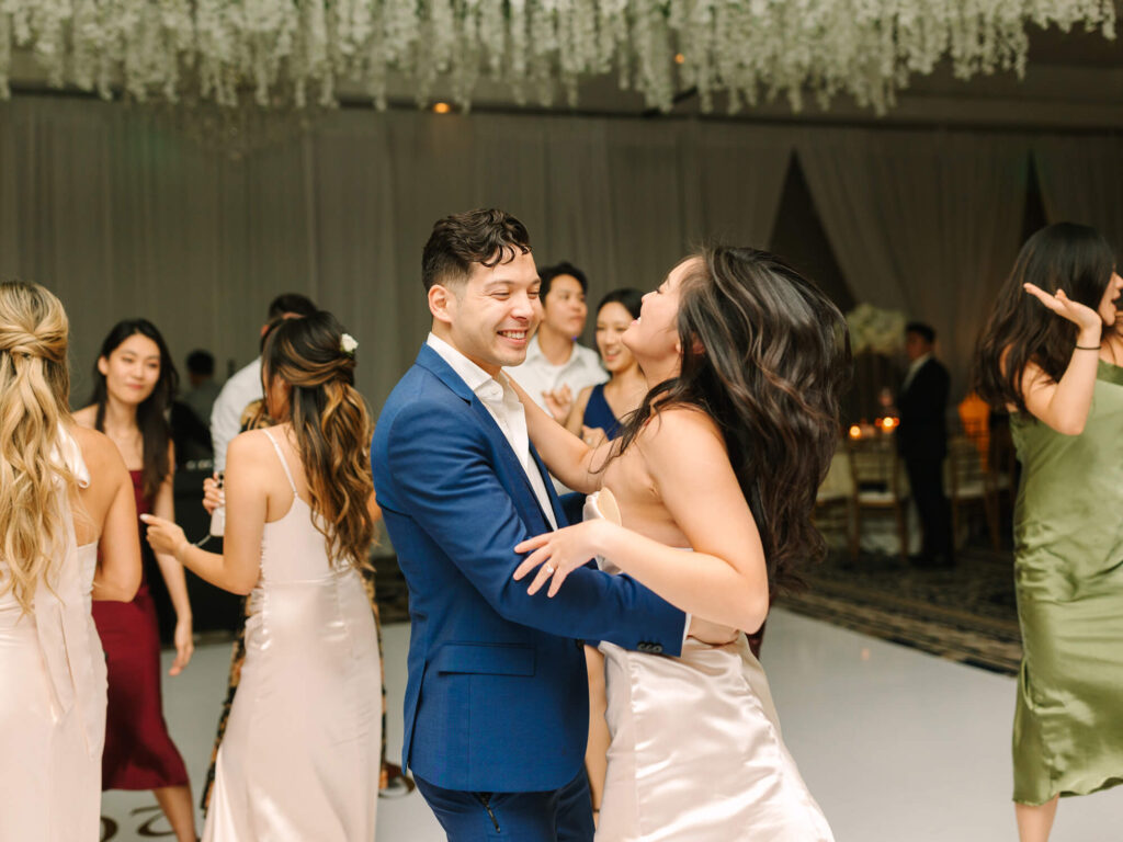 A joyful couple dances exuberantly at a wedding, surrounded by smiling guests.