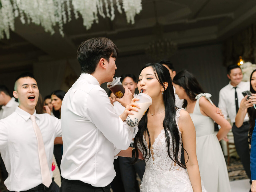 A joyful wedding scene with a bride and groom sharing bubble boba tea, surrounded by cheering friends.