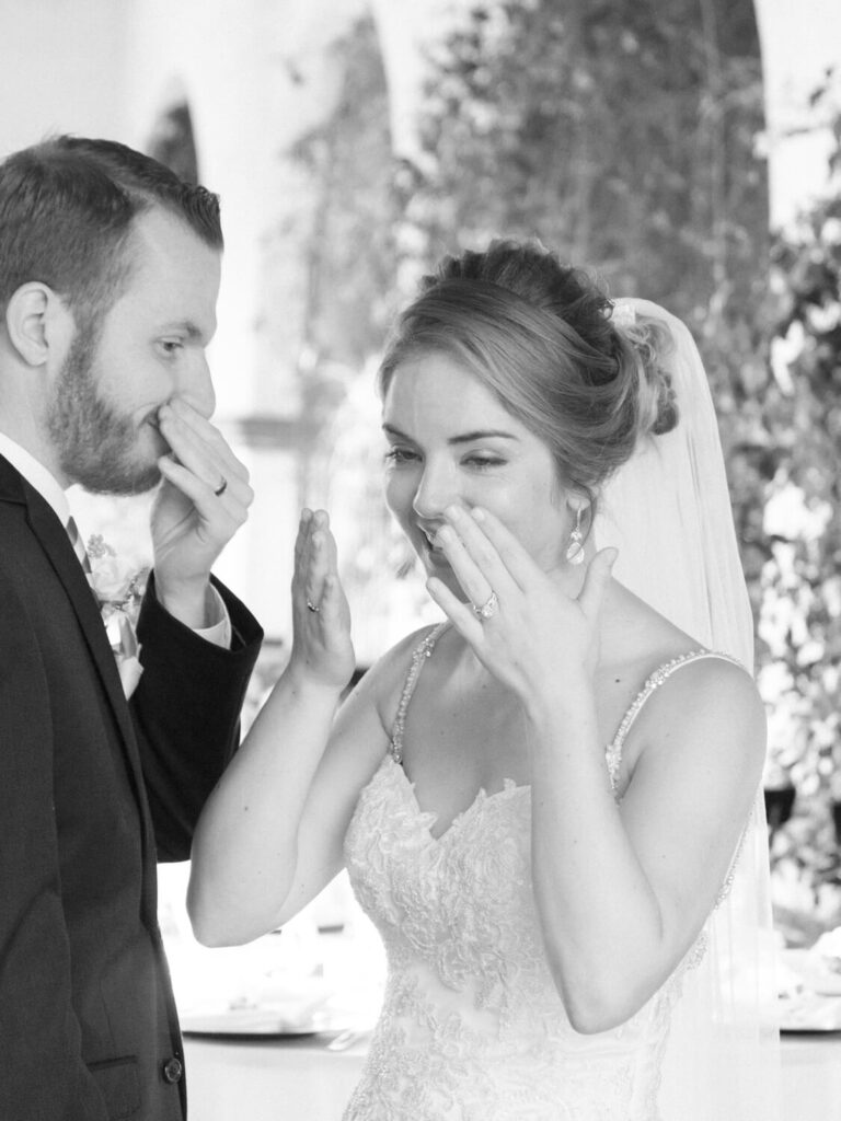 A bride and groom share an emotional moment, both wiping tears from their eyes.