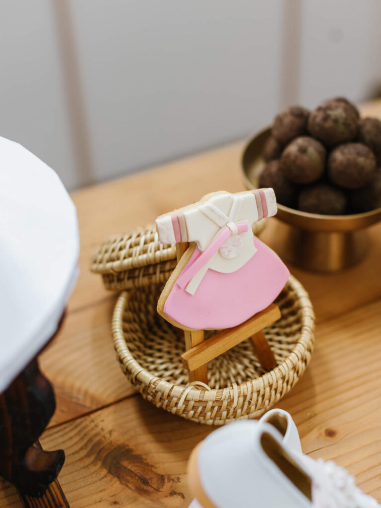 A pink and white hanbok-shaped cookie on a small wooden easel, placed in a wicker basket on a wooden table. A bowl of round rice balls is in the background.