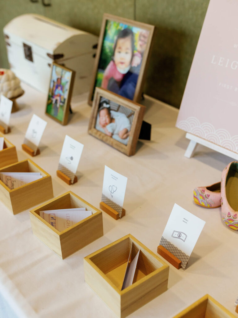 A display table with wooden boxes, each holding cards with simple line drawings. Framed baby photos and colorful baby shoes add warmth.